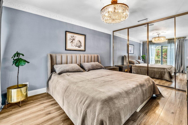 bedroom with a closet, wood-type flooring, ornamental molding, and an inviting chandelier