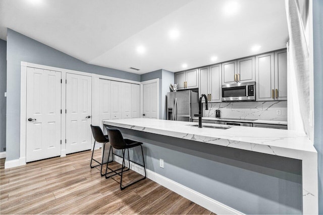 kitchen featuring a breakfast bar area, light stone countertops, gray cabinetry, and stainless steel appliances