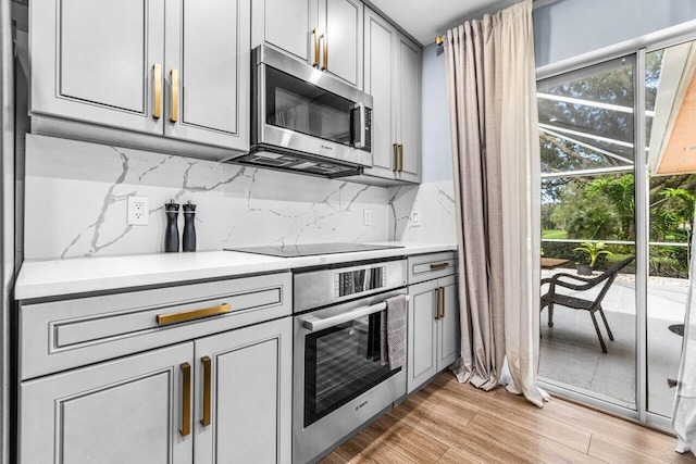 kitchen with gray cabinets, decorative backsplash, stainless steel appliances, and light hardwood / wood-style floors