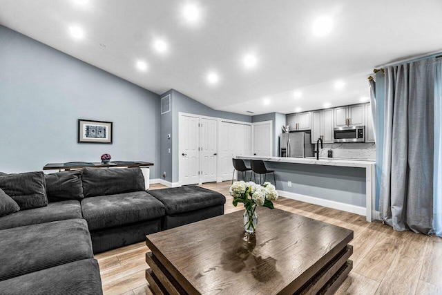 living room featuring lofted ceiling, sink, and light wood-type flooring