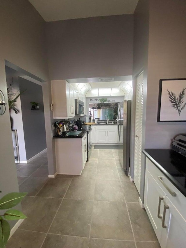 kitchen featuring appliances with stainless steel finishes, sink, white cabinetry, a high ceiling, and light tile patterned floors