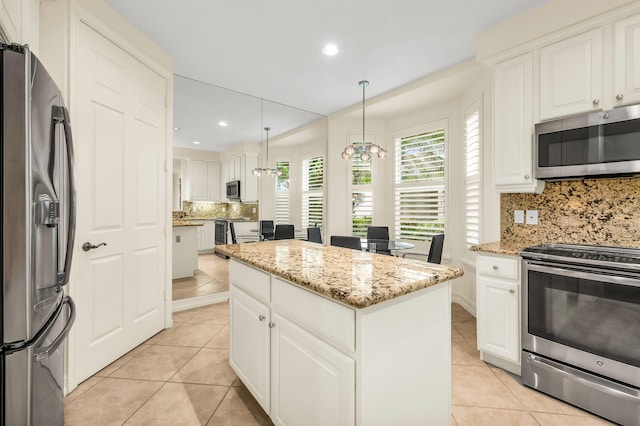 kitchen featuring pendant lighting, light stone counters, decorative backsplash, appliances with stainless steel finishes, and a center island