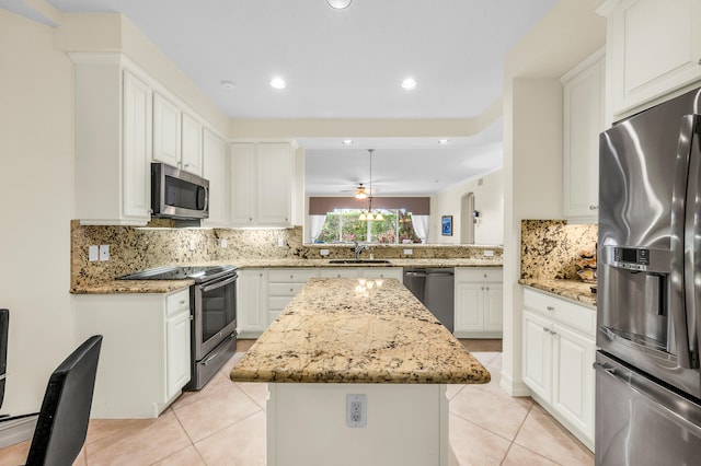 kitchen featuring sink, stainless steel appliances, light stone countertops, white cabinets, and a center island