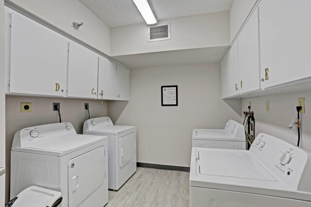 laundry room featuring a textured ceiling, light hardwood / wood-style flooring, washing machine and clothes dryer, and cabinets