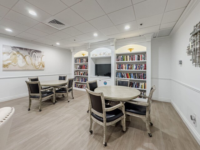 dining space with ornamental molding, light hardwood / wood-style flooring, a paneled ceiling, and built in features