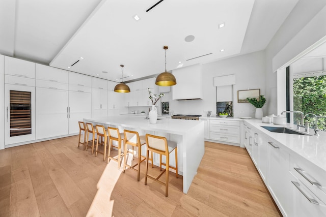 kitchen with a breakfast bar, a kitchen island with sink, white cabinets, sink, and decorative light fixtures