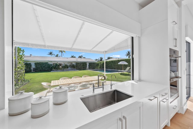 kitchen featuring white cabinetry, sink, light hardwood / wood-style flooring, double oven, and vaulted ceiling