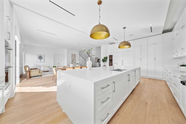 kitchen featuring a kitchen island with sink, white cabinets, sink, decorative light fixtures, and light hardwood / wood-style floors