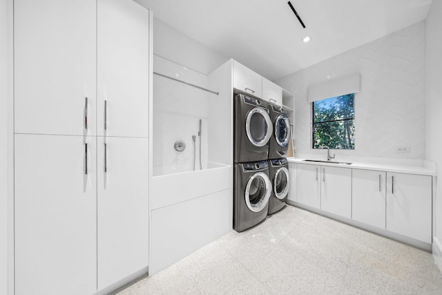 clothes washing area featuring sink, cabinets, and stacked washer and dryer