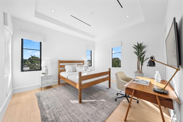 bedroom with multiple windows, light hardwood / wood-style flooring, and a tray ceiling