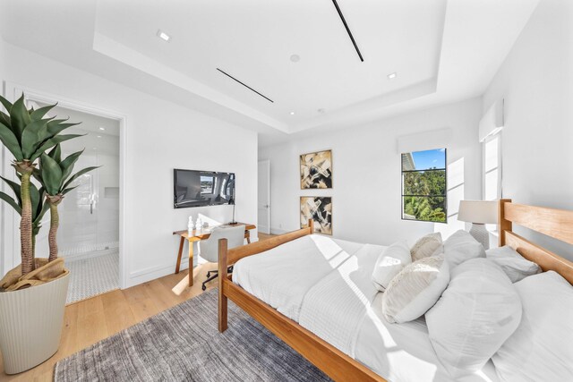 bedroom featuring ensuite bathroom, light hardwood / wood-style floors, and a raised ceiling