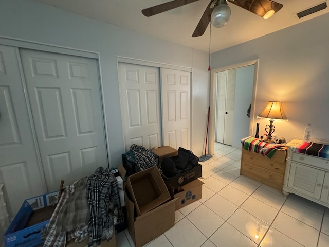 bedroom with ceiling fan, light tile patterned flooring, and two closets