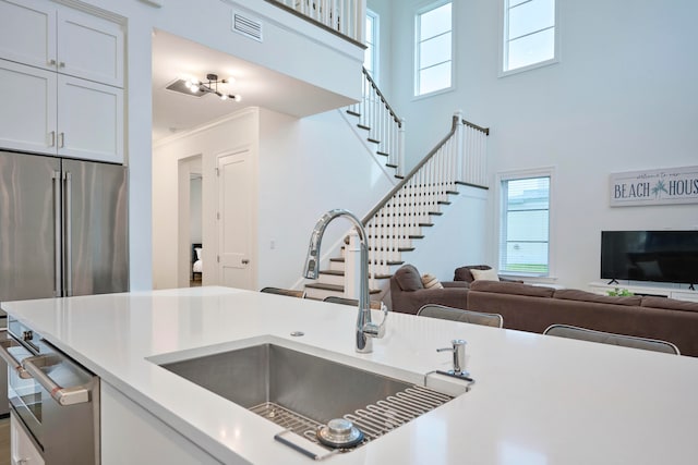 kitchen with white cabinetry, crown molding, a towering ceiling, and a wealth of natural light