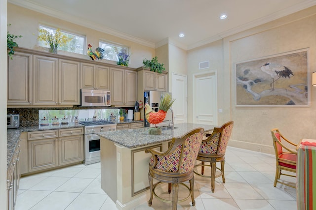 kitchen with light stone countertops, a kitchen island with sink, ornamental molding, appliances with stainless steel finishes, and a kitchen bar