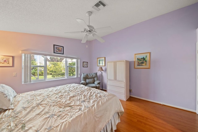 bedroom featuring lofted ceiling, light hardwood / wood-style flooring, a textured ceiling, and ceiling fan