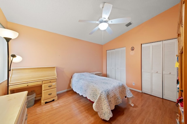 bedroom with vaulted ceiling, two closets, light hardwood / wood-style floors, and ceiling fan