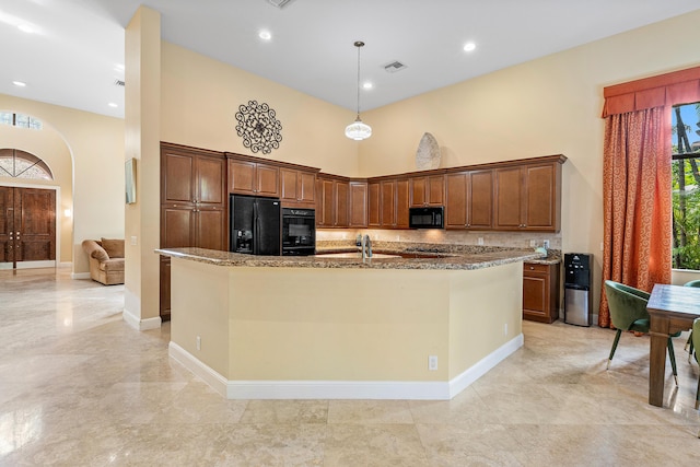 kitchen featuring black appliances, a towering ceiling, a kitchen island with sink, and hanging light fixtures