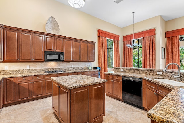 kitchen featuring light stone counters, sink, black appliances, pendant lighting, and a center island