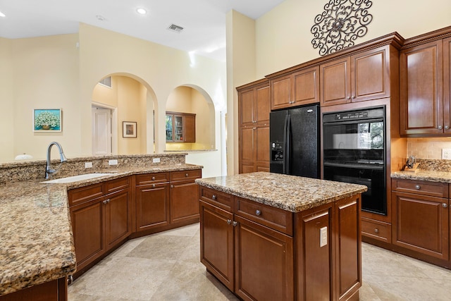 kitchen with sink, a center island, light stone countertops, and black appliances