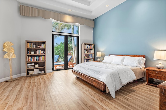 bedroom featuring access to exterior, light wood-type flooring, a towering ceiling, and french doors