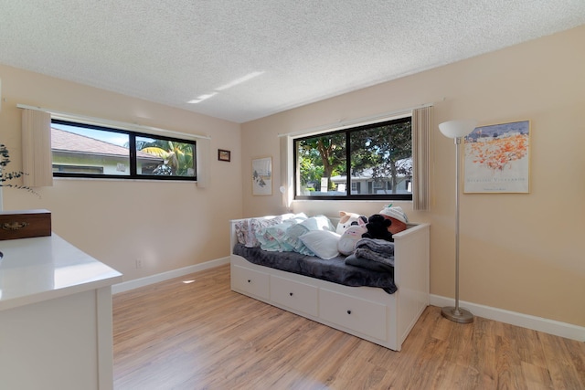 bedroom featuring light hardwood / wood-style floors, multiple windows, and a textured ceiling