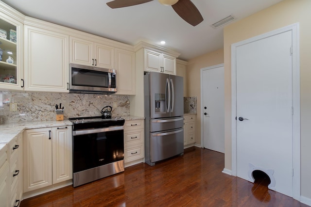 kitchen with decorative backsplash, light stone counters, dark wood-type flooring, cream cabinetry, and stainless steel appliances