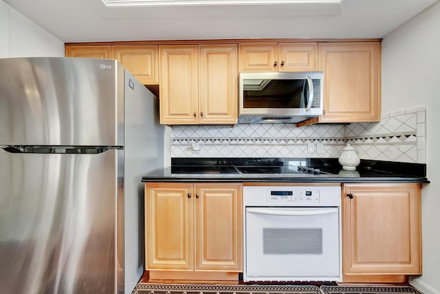 kitchen with light brown cabinets, appliances with stainless steel finishes, dark stone counters, and tasteful backsplash