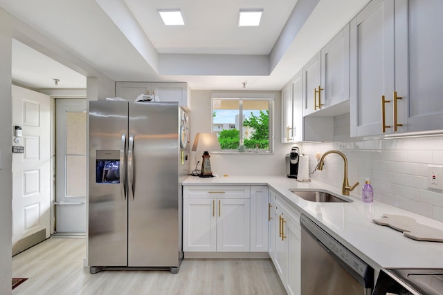 kitchen featuring a tray ceiling, sink, white cabinets, light wood-type flooring, and appliances with stainless steel finishes