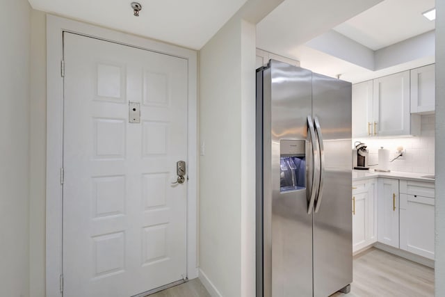 kitchen with stainless steel fridge, white cabinetry, light wood-type flooring, and tasteful backsplash