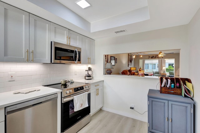 kitchen featuring white cabinets, ceiling fan, backsplash, light hardwood / wood-style flooring, and stainless steel appliances