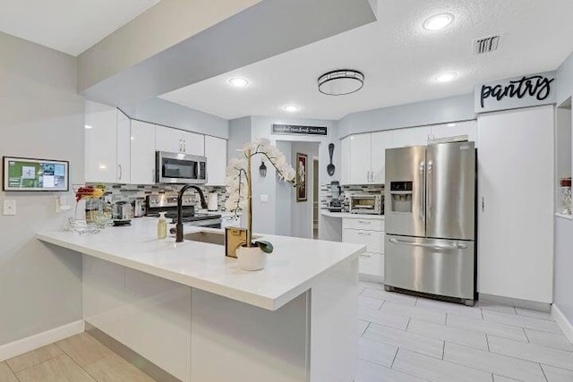 kitchen featuring kitchen peninsula, tasteful backsplash, a textured ceiling, white cabinetry, and appliances with stainless steel finishes