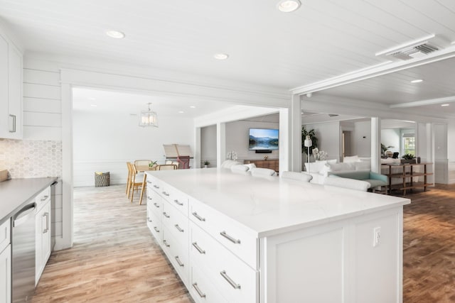 kitchen with stainless steel dishwasher, a kitchen island, light stone countertops, white cabinetry, and light hardwood / wood-style flooring