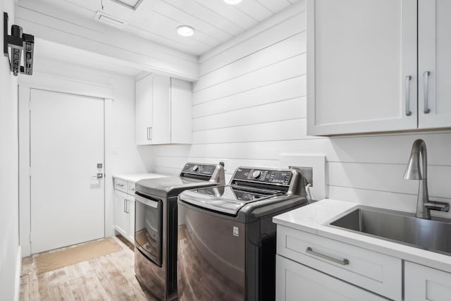 washroom with cabinets, wood walls, sink, washing machine and clothes dryer, and light hardwood / wood-style flooring