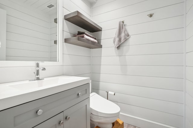 bathroom with toilet, wood walls, vanity, and wood-type flooring