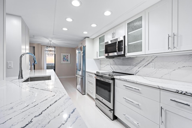 kitchen with light stone countertops, appliances with stainless steel finishes, tasteful backsplash, sink, and white cabinetry