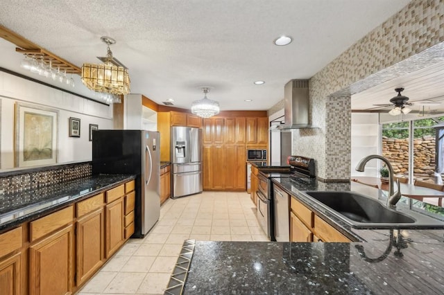 kitchen with sink, pendant lighting, dark stone counters, wall chimney range hood, and appliances with stainless steel finishes