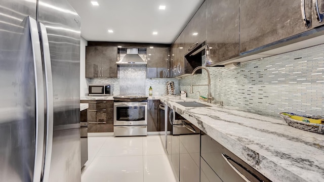 kitchen featuring sink, wall chimney exhaust hood, light stone countertops, appliances with stainless steel finishes, and light tile patterned flooring