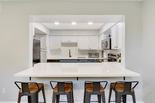 kitchen with kitchen peninsula, a breakfast bar area, stainless steel appliances, and white cabinets