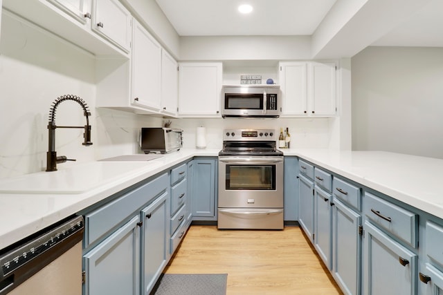 kitchen featuring light wood-type flooring, blue cabinetry, sink, appliances with stainless steel finishes, and white cabinetry