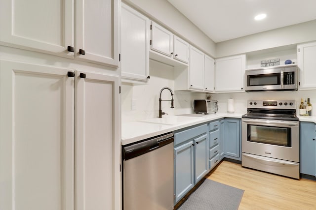 kitchen with sink, white cabinetry, blue cabinetry, appliances with stainless steel finishes, and light hardwood / wood-style floors