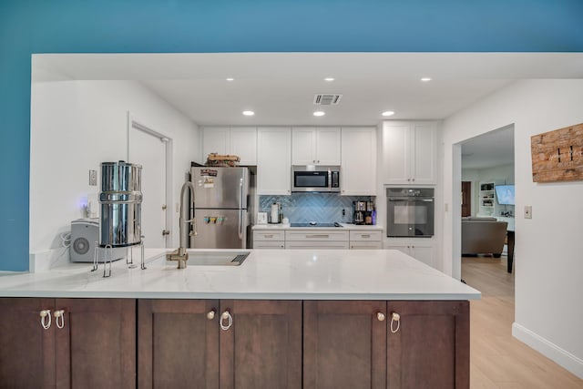 kitchen with a peninsula, visible vents, white cabinets, backsplash, and black appliances