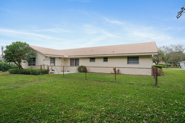 rear view of house featuring a yard, fence, and stucco siding