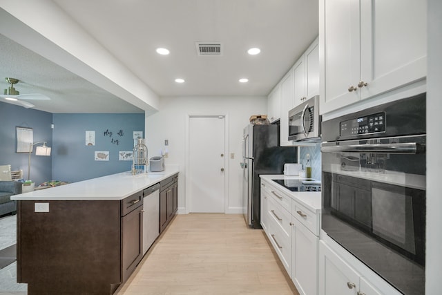 kitchen featuring light wood finished floors, a peninsula, black appliances, white cabinetry, and a sink