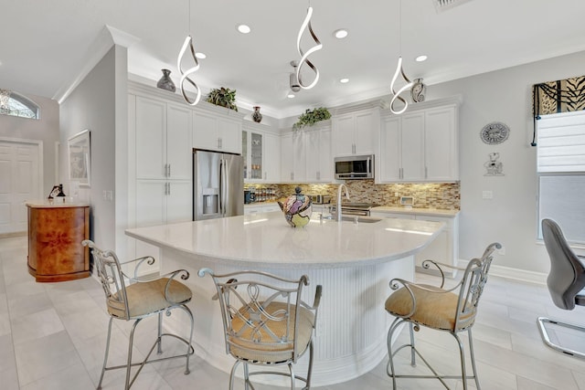 kitchen with stainless steel appliances, hanging light fixtures, a center island with sink, and white cabinetry