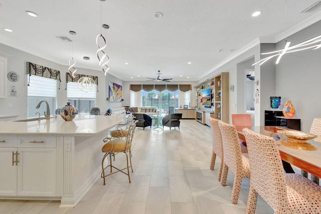 kitchen featuring ceiling fan, a kitchen island with sink, white cabinets, crown molding, and decorative light fixtures