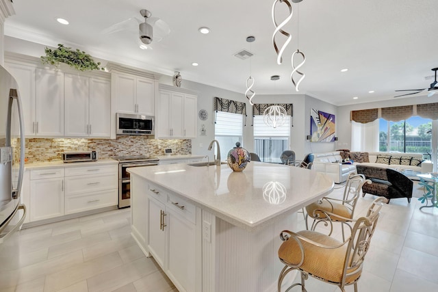 kitchen with ceiling fan, ornamental molding, a center island with sink, white cabinetry, and appliances with stainless steel finishes