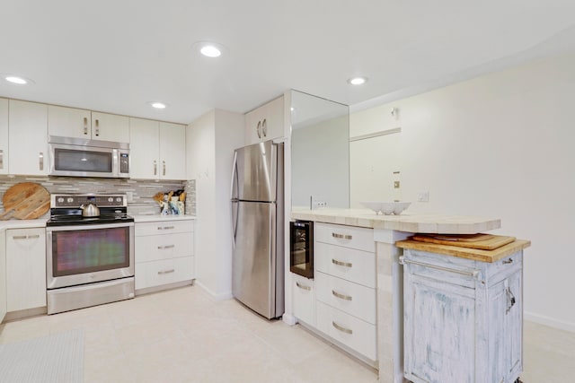 kitchen with light tile patterned flooring, backsplash, white cabinets, and appliances with stainless steel finishes