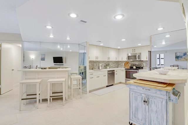 kitchen with decorative backsplash, white cabinets, sink, kitchen peninsula, and appliances with stainless steel finishes