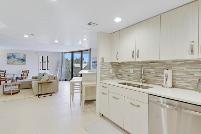 kitchen with decorative backsplash, stainless steel dishwasher, sink, a kitchen bar, and light tile patterned floors