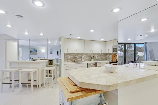 kitchen featuring decorative backsplash, white cabinetry, sink, and a breakfast bar